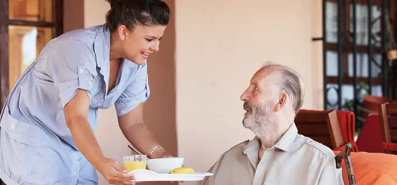 Elderly woman smiling as she holds hands with her home care provider